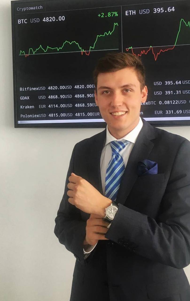 Danila in a suit in front of a live crypto price screen